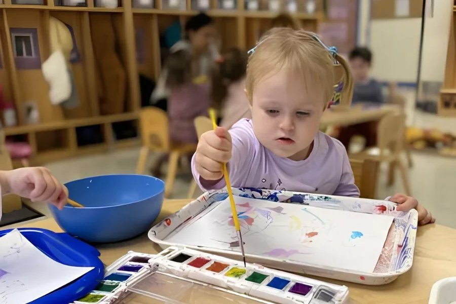 little girl painting with water colors in classroom