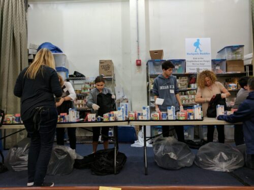 Volunteers on the assembly line placing items of food into the backpacks.