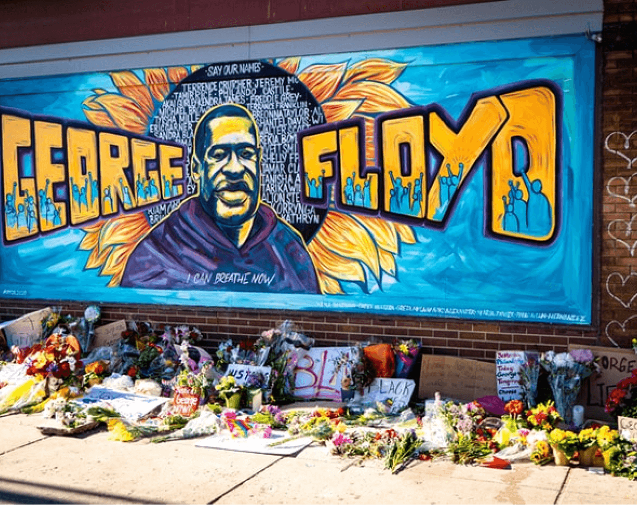 mural honoring the memory of george floyd with flowers and signs on the sidewalk underneath the mural