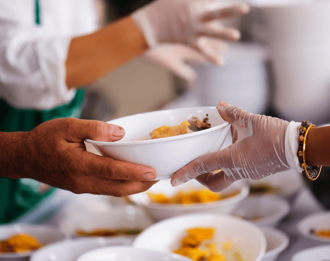 close up of the hands of a person with a gloved hand handing a bowl of food to the hand of another person without a glove