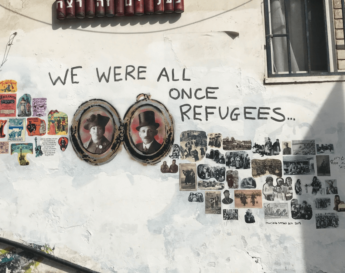 graffiti art on the wall of a building with the words, we were all once refugees and images of immigrant families, pasted to the wall