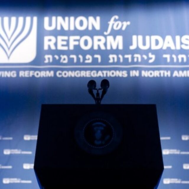 Empty Podium in silhouette in front of a Union For Reform Judaism logo banner in hebrew and english and a step and repeat with the logo