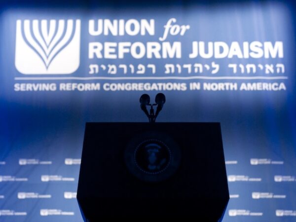 Empty Podium in silhouette in front of a Union For Reform Judaism logo banner in hebrew and english and a step and repeat with the logo